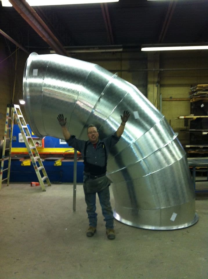 A Local 397 member standing with a fabricated 65-inch sheet metal elbow in the shop